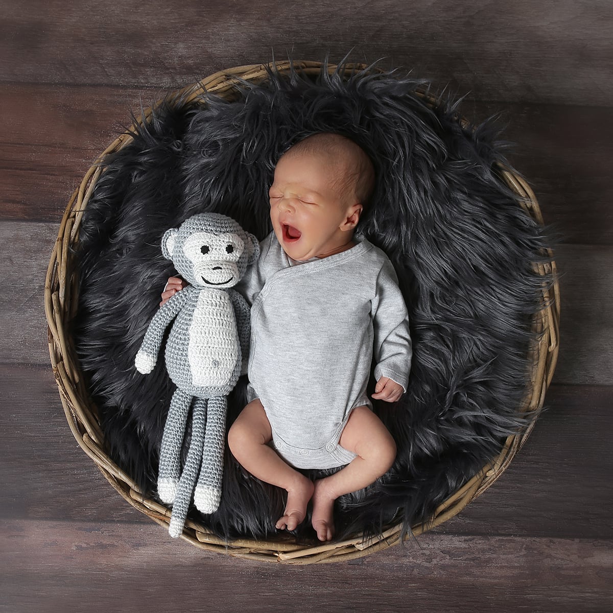 Ein Baby mit einem Affen-Stofftier, das gerade am gähnen ist und in einem Fell liegt